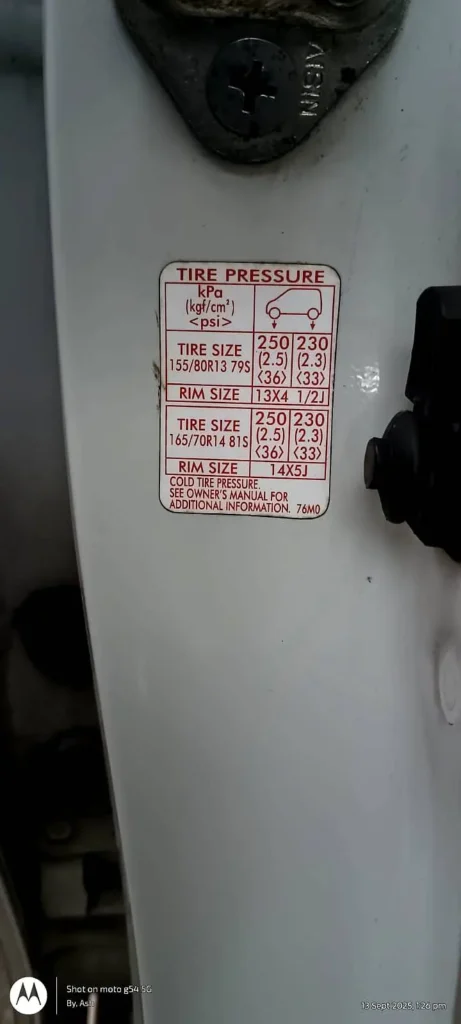 Close-up photograph of a white car's tire pressure information sticker located on the driver's side door jamb. The sticker shows tire pressure specifications